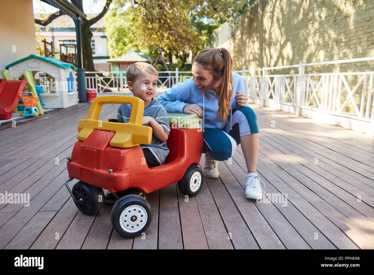 Kindergarten teacher and a boy in a pedal car on the terrace of Kita or