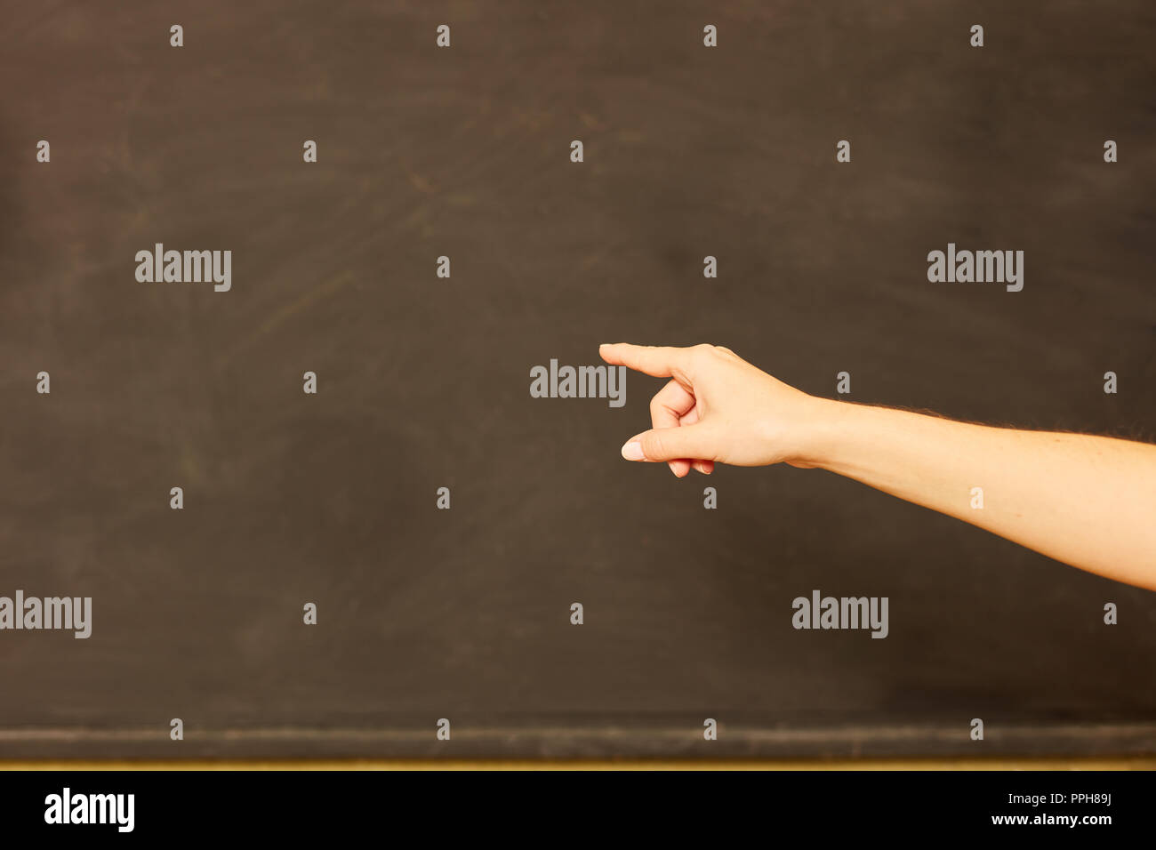 Hand of a teacher points to an empty blackboard as a sign of education Stock Photo