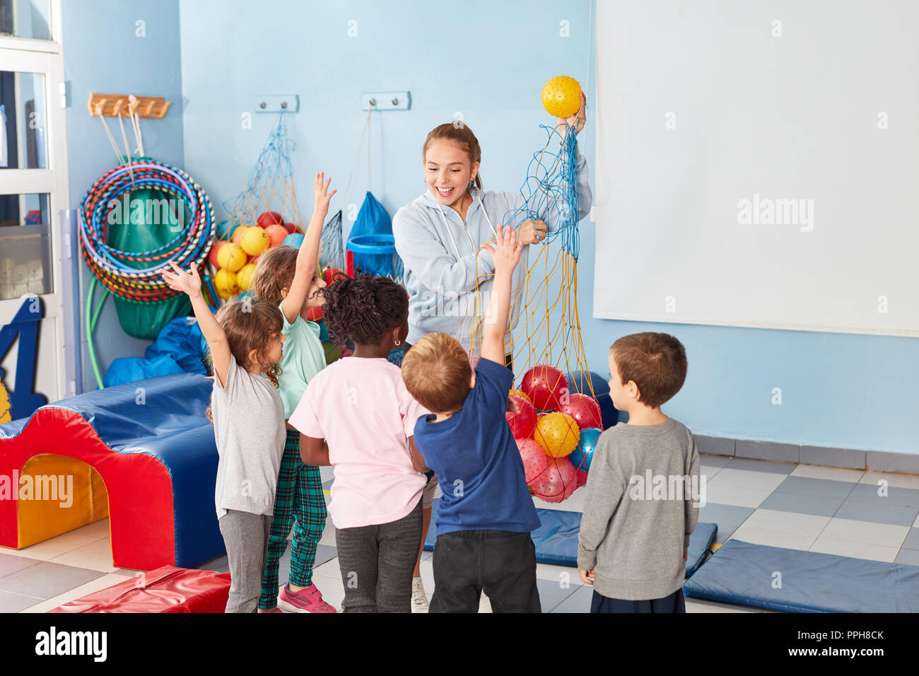 Sports teacher and children in the gymnasium of elementary school are looking forward to ball game Stock Photo