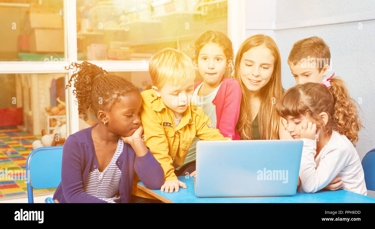 Kids play together at laptop computer with educator in kindergarten