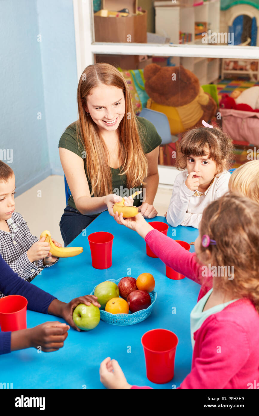 Woman as an educator and children in the daycare eat fruit at the snack in the cafeteria Stock