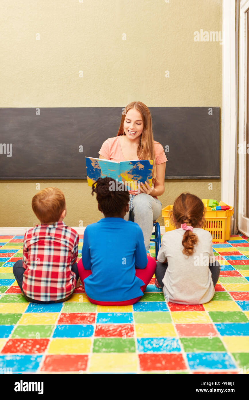Woman as a kindergarten teacher and children reading from a children's book in kindergarten Stock Photo