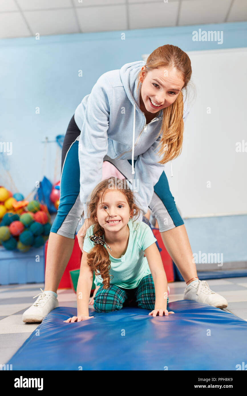 Woman as a sports teacher helps girl while doing gymnastics in the gym in elementary school Stock Photo