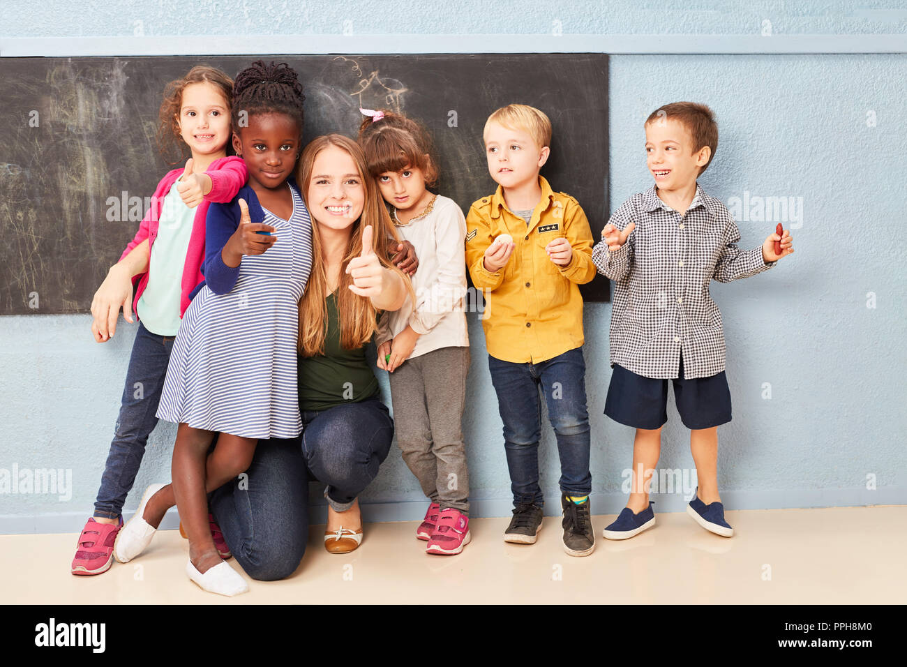Group of kids as a student and teacher keep their thumbs up in elementary school Stock Photo