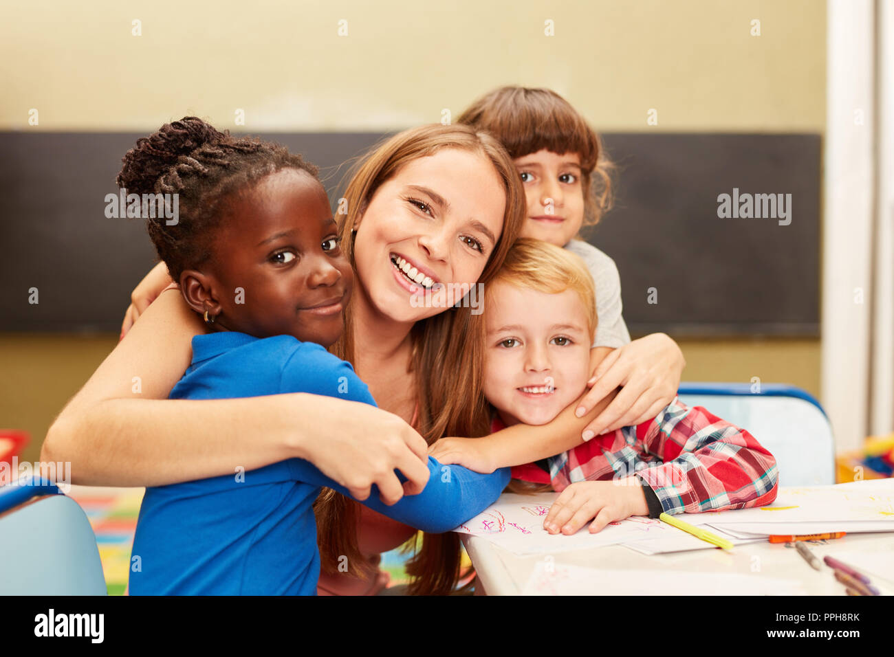 Happy children as a student hug their educator in kindergarten or school Stock Photo