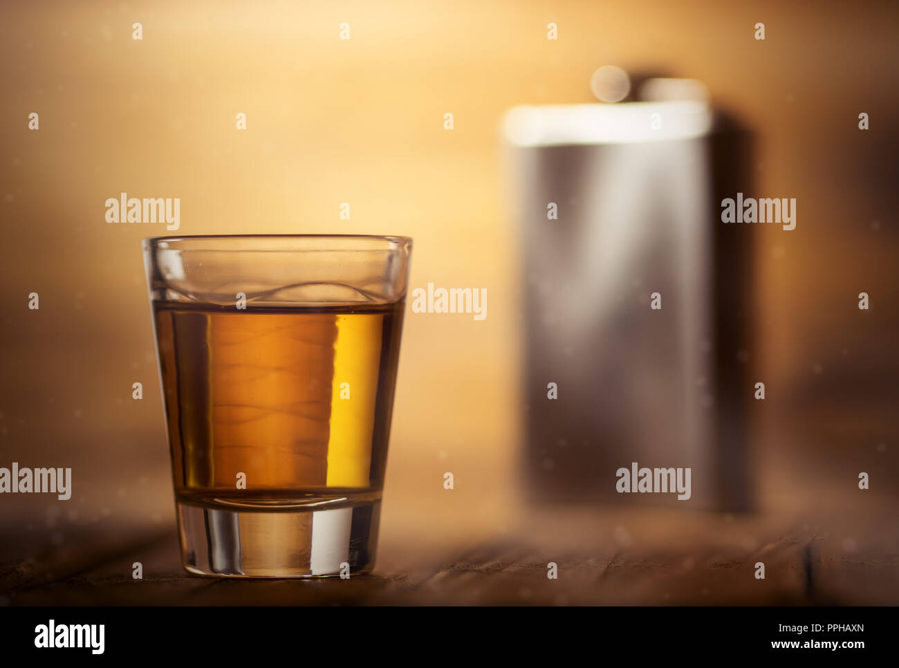 Metal whiskey hip flask closeup, on a wooden table, with a shot glass