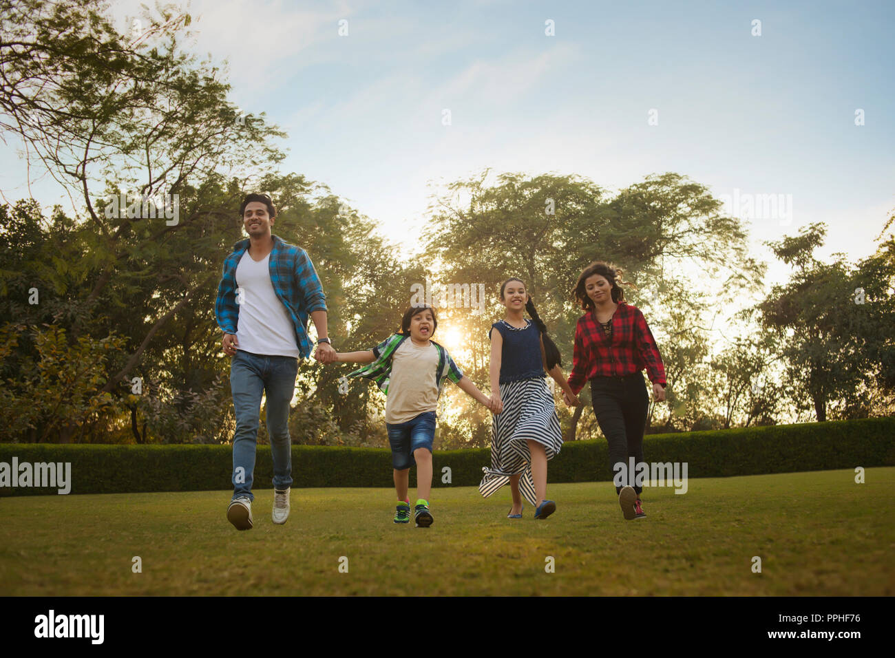 Happy family of man woman son and daughter walking in park holding hands. Stock Photo