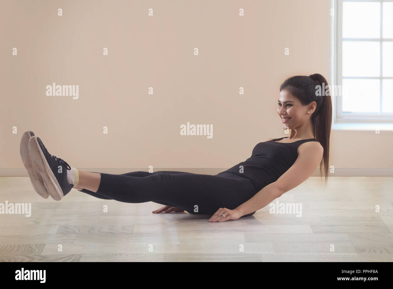 Smiling young woman in workout clothes doing abs exercises on the floor. Stock Photo