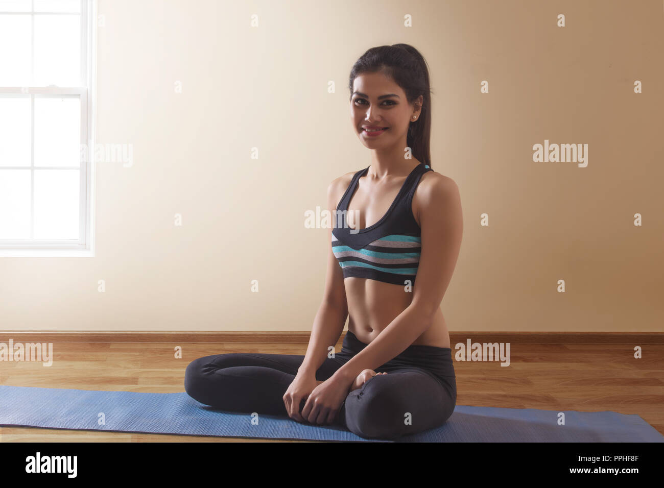 Young woman in workout clothes sitting on yoga mat. Stock Photo
