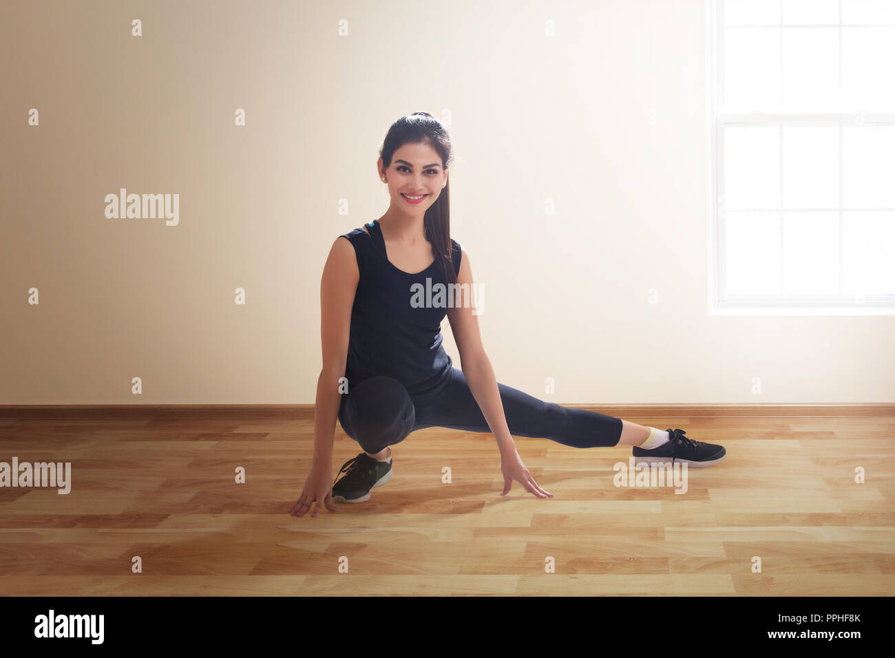 Young woman in workout clothes doing leg stretching exercises on the floor. Stock Photo