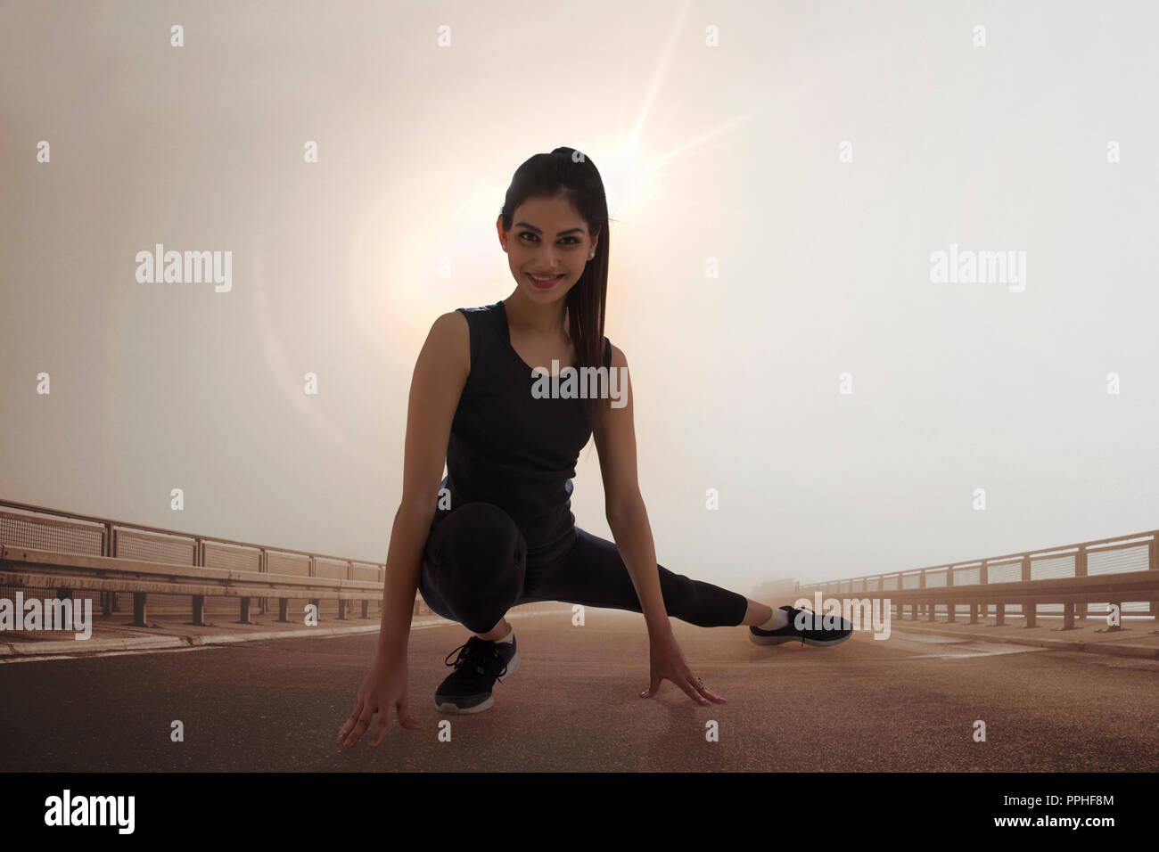 Young woman in workout clothes doing stretching exercises outdoors with sun in the background. Stock Photo