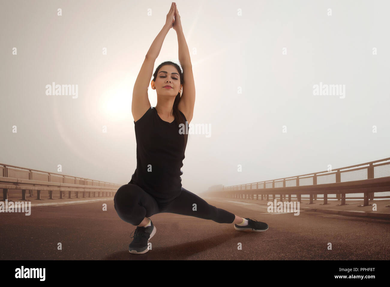 Young woman in workout clothes doing yoga outdoors with sun in the background. Stock Photo