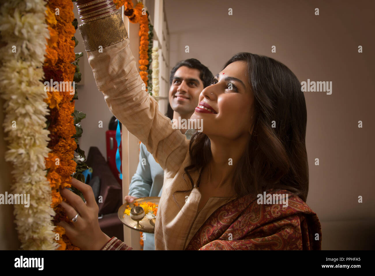 Close up of happy young couple in traditional dress decorating their home with flowers. Stock Photo