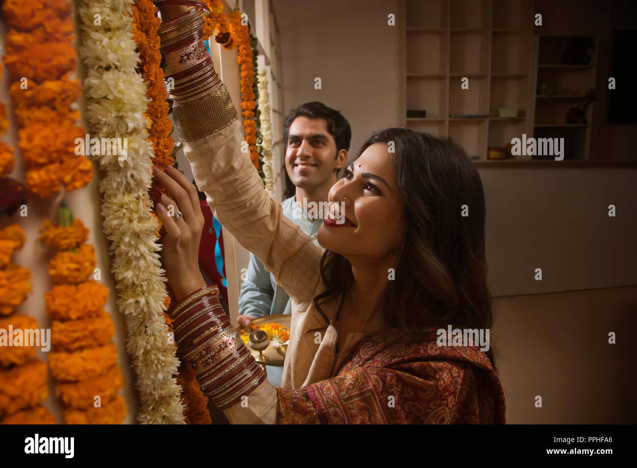 Close up of happy young couple in traditional dress decorating their home with flowers. Stock Photo