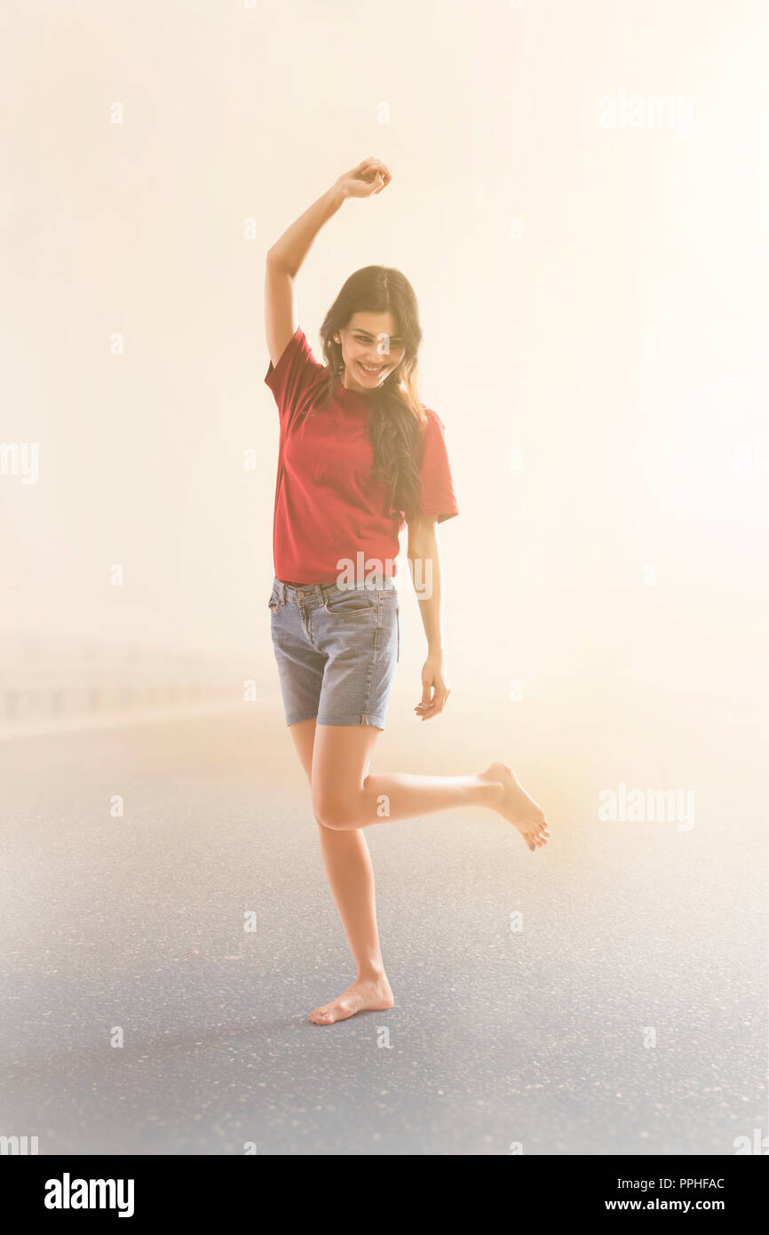 Young woman dancing joyfully on the road against foggy background. Stock Photo