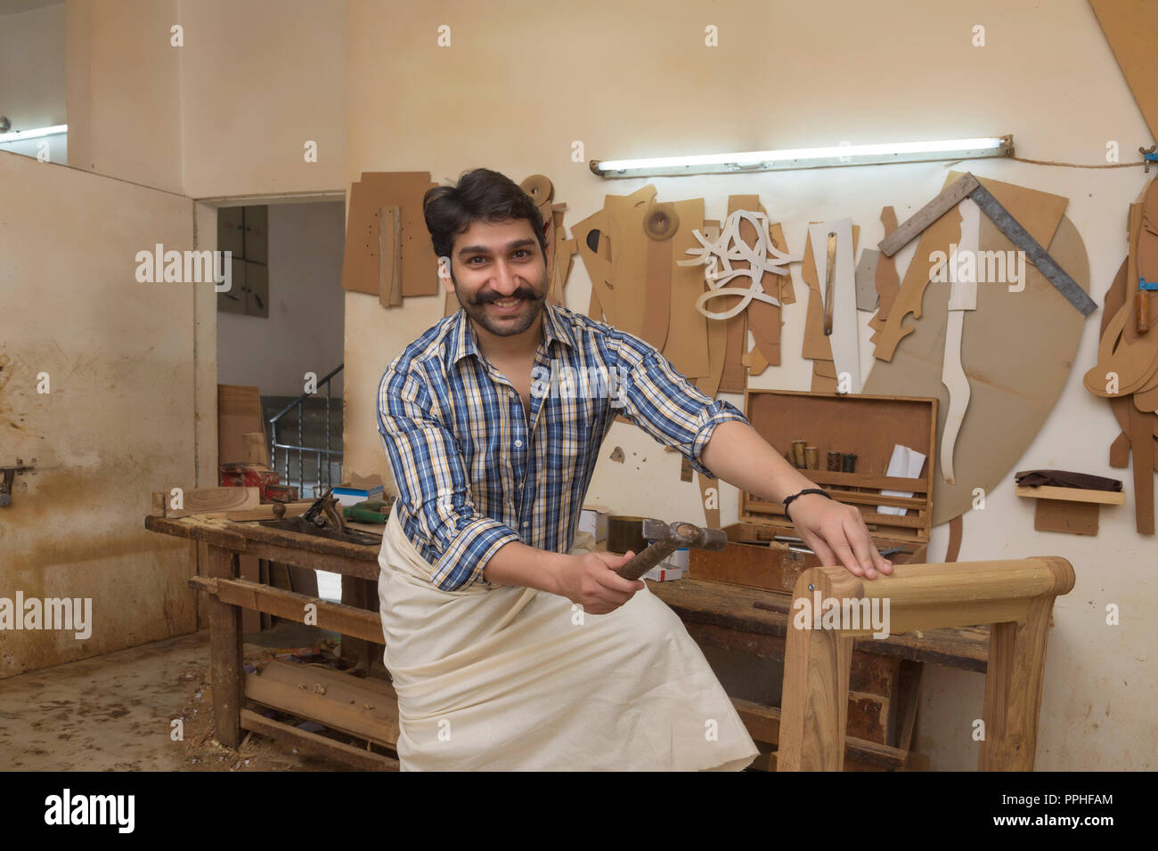 Happy carpenter hitting a nail with hammer in his workshop. Stock Photo