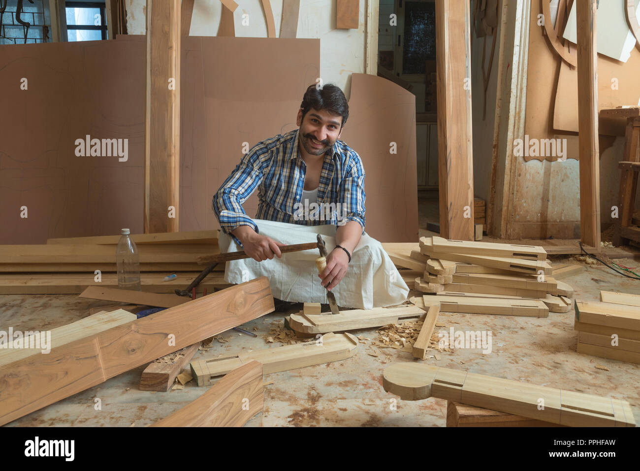 Happy looking carpenter working with a chisel and hammer sitting in his workshop. Stock Photo