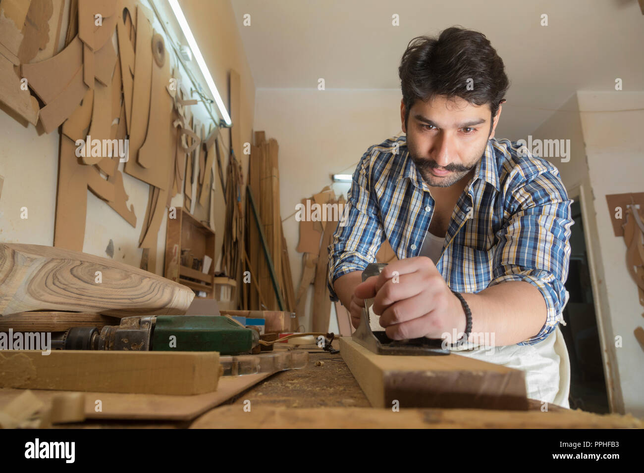 Carpenter using a scraper blade to smoothen wooden log on his work bench. Stock Photo