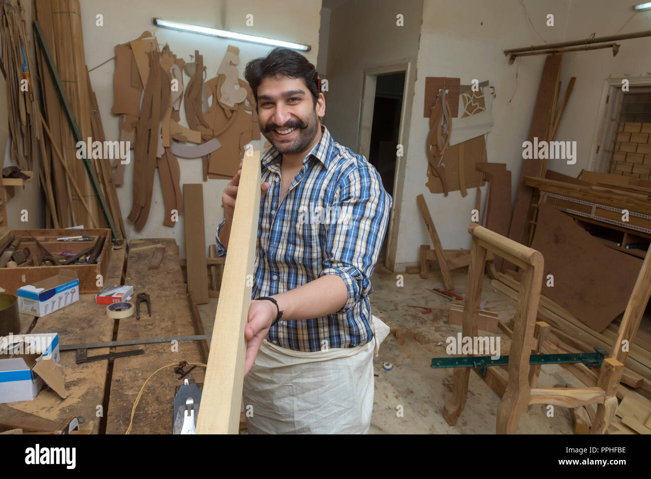 Smiling carpenter in his workshop checking the straightness of a wooden log. Stock Photo