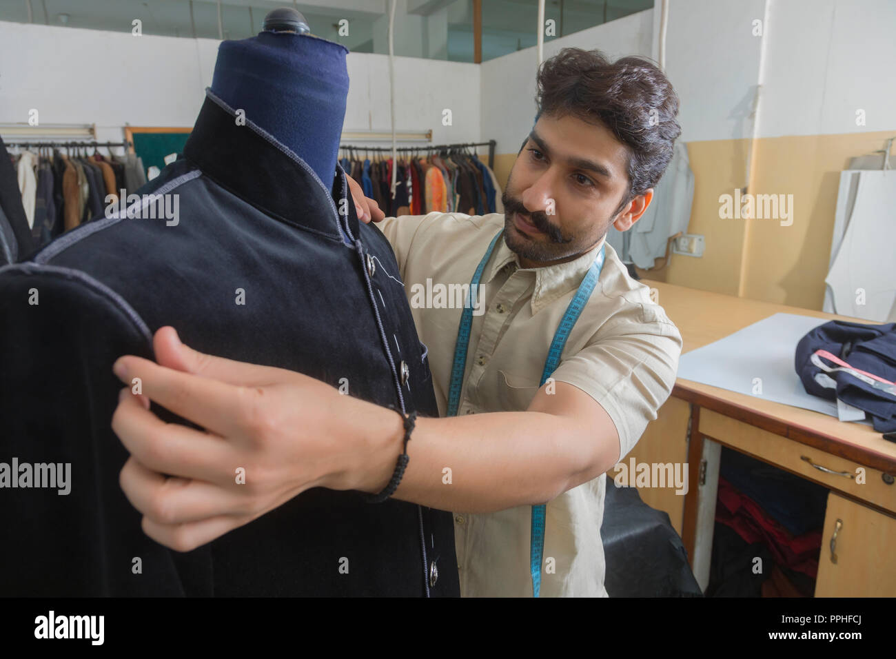 Tailor putting a semi-stitched coat on a mannequin in his workshop to check the fitting. Stock Photo