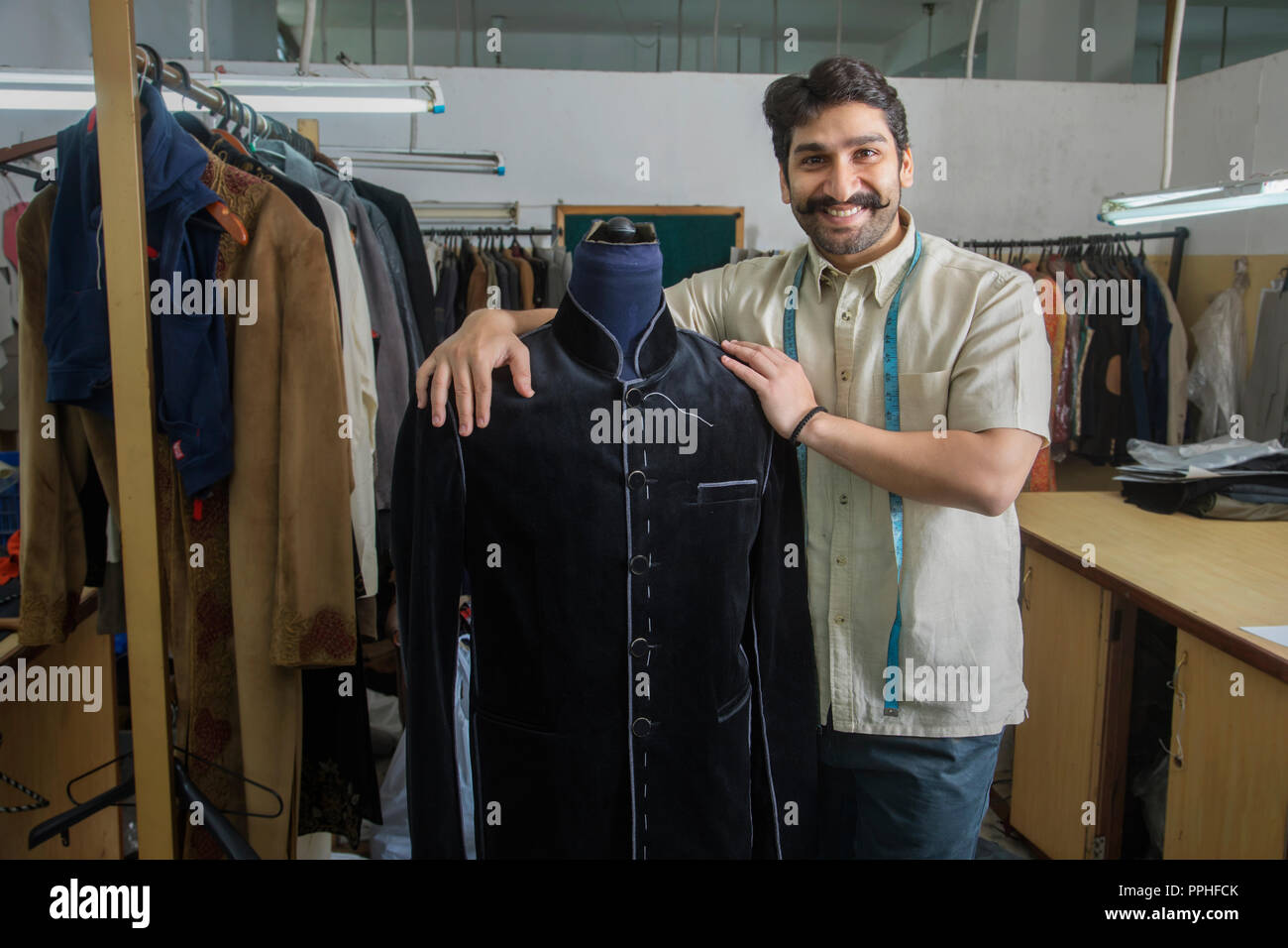 Tailor standing beside a mannequin wearing a semi-stitched coat in his workshop. Stock Photo