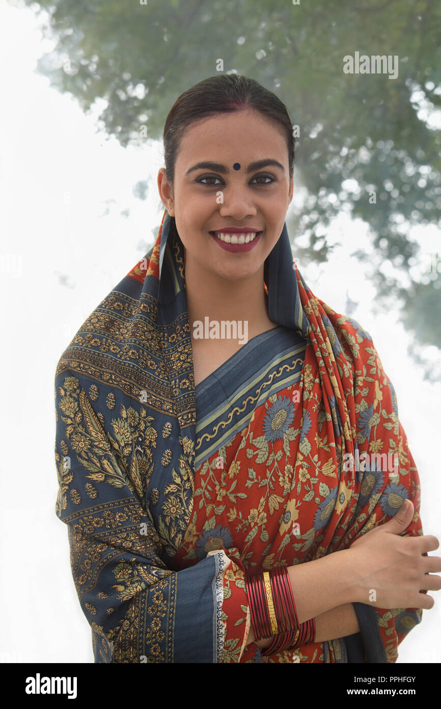 Portrait of a smiling village woman in saree standing with arms crossed. Stock Photo