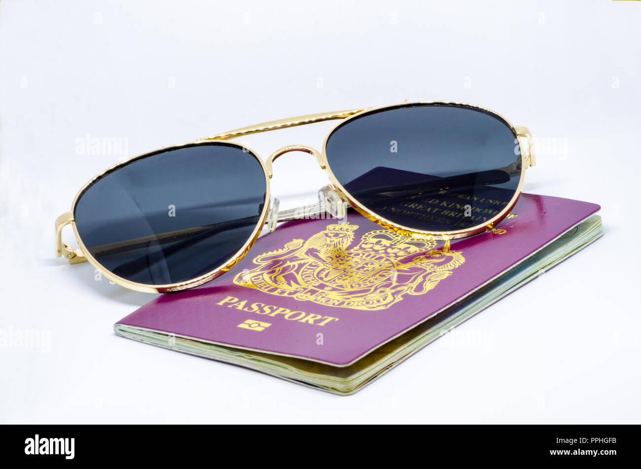 Holiday and Travel Concept - A red, burgundy, British European passport and a pair of sunglasses on a white background. Stock Photo