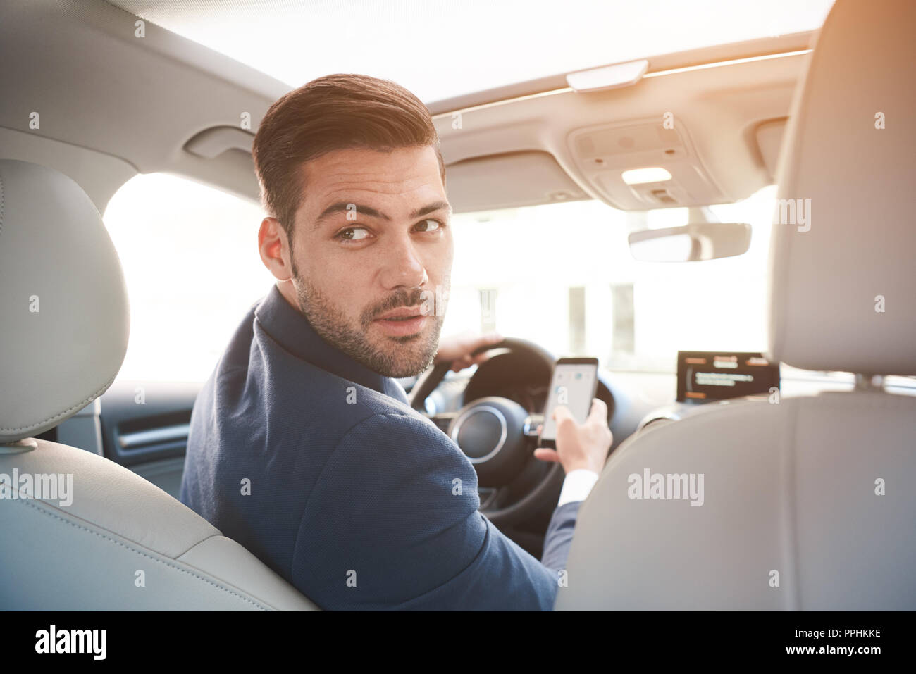 Portrait of stylish confident businessman in car wearing black suit