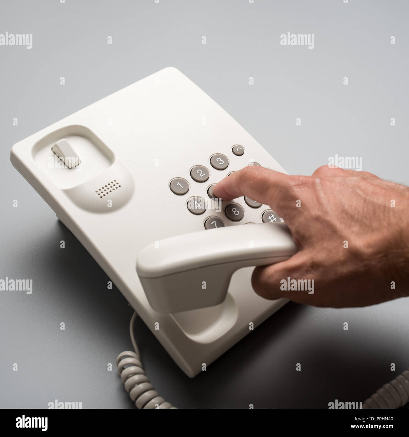 Male hand dialing telephone number using white landline phone, over grey background. Stock Photo