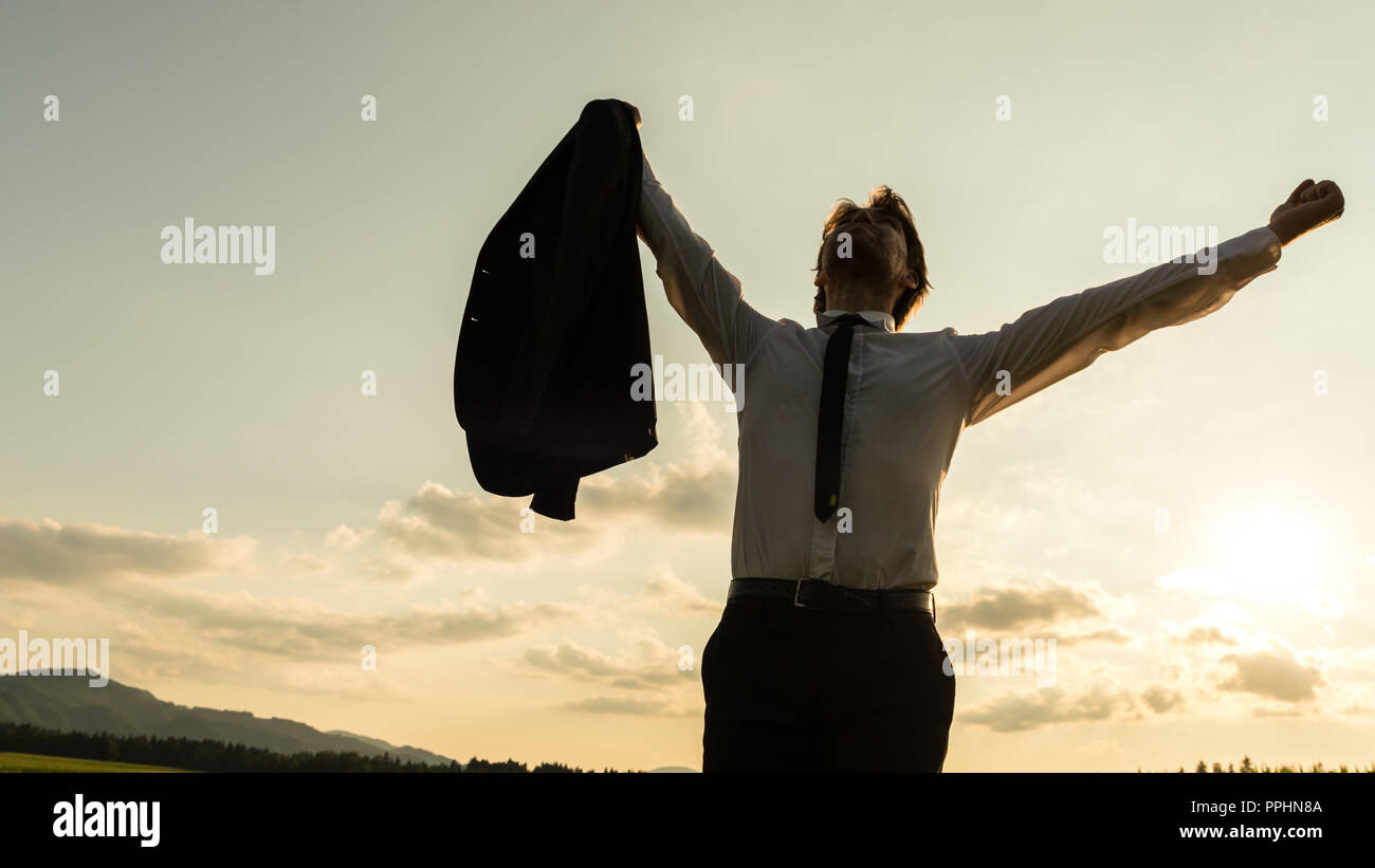 Businessman standing in evening nature with his arms raised up high in ...