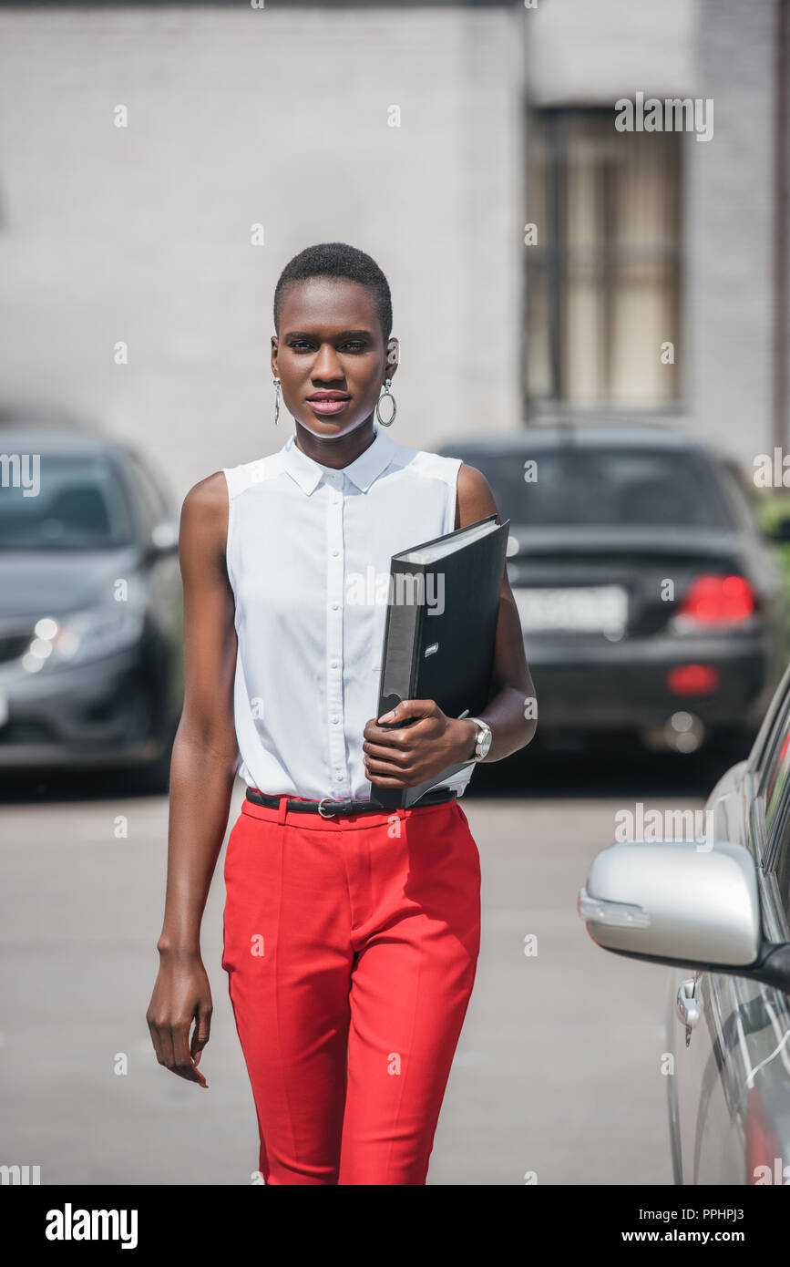 stylish attractive african american businesswoman walking near car on ...