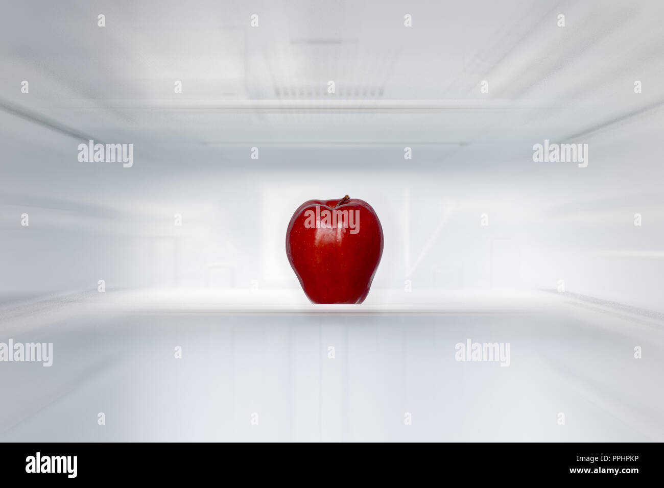 A lone red apple on a shelf in an empty fridge. One fresh apple in an