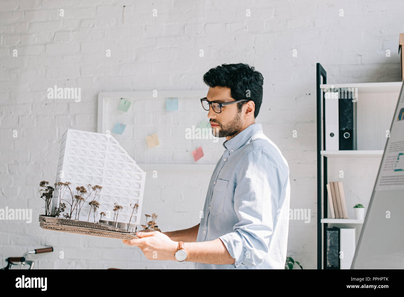 side view of handsome architect in glasses holding architecture model in office Stock Photo