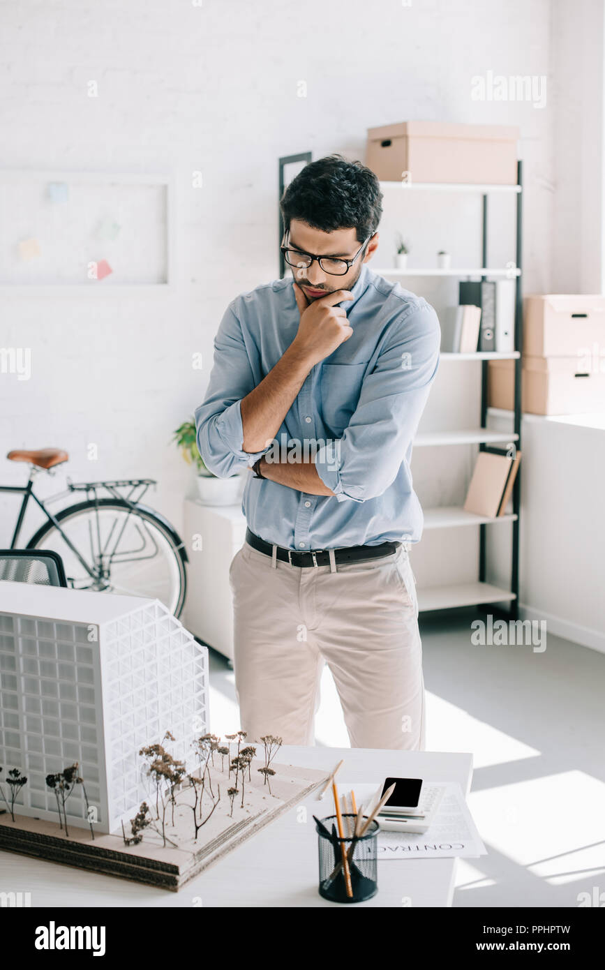 pensive handsome architect looking at architecture model on table in office Stock Photo