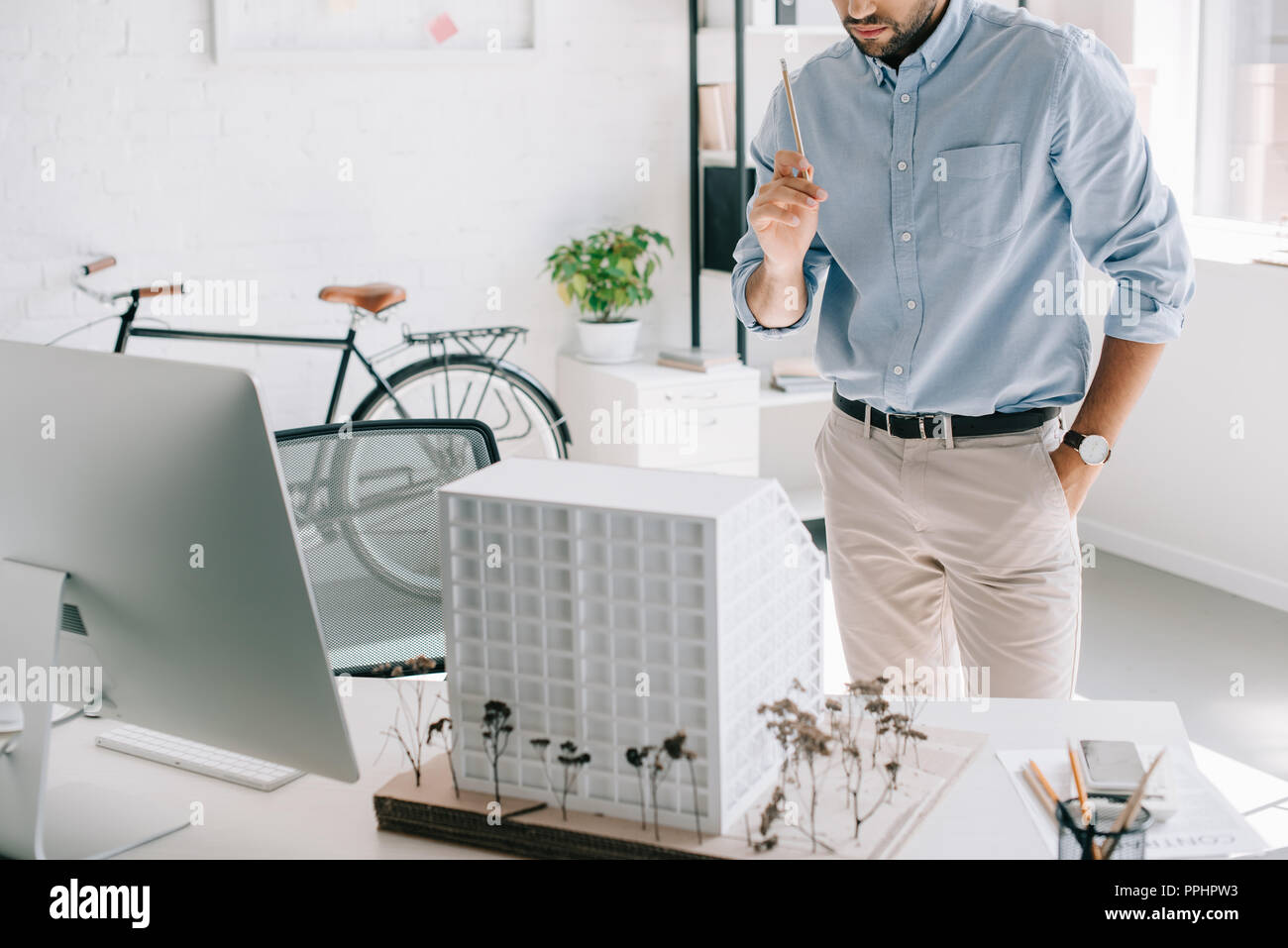 cropped image of architect holding pencil and standing near architecture model on table in office Stock Photo