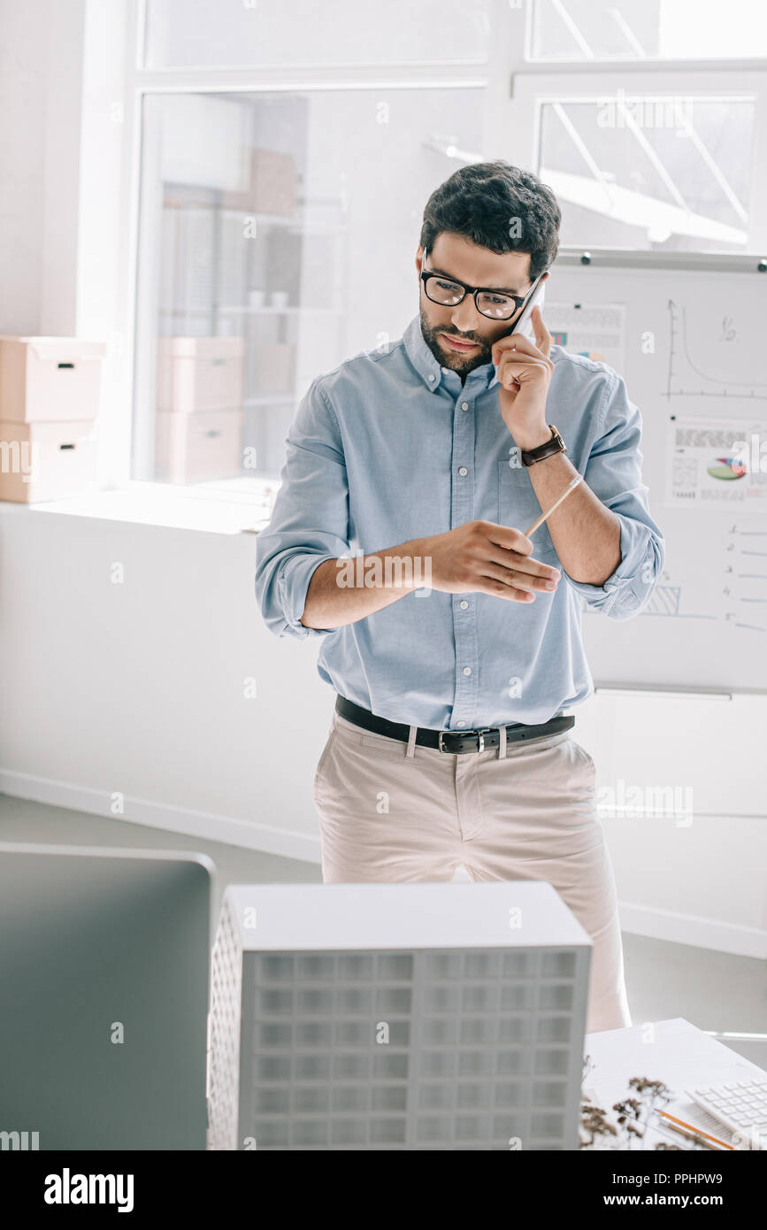 handsome architect talking by smartphone and looking at architecture model in office Stock Photo