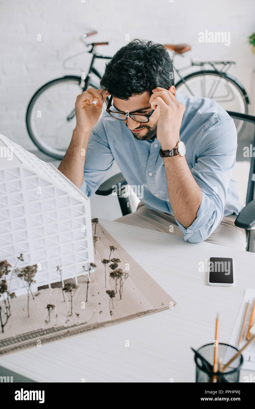 handsome architect touching head and looking at architecture model in office Stock Photo