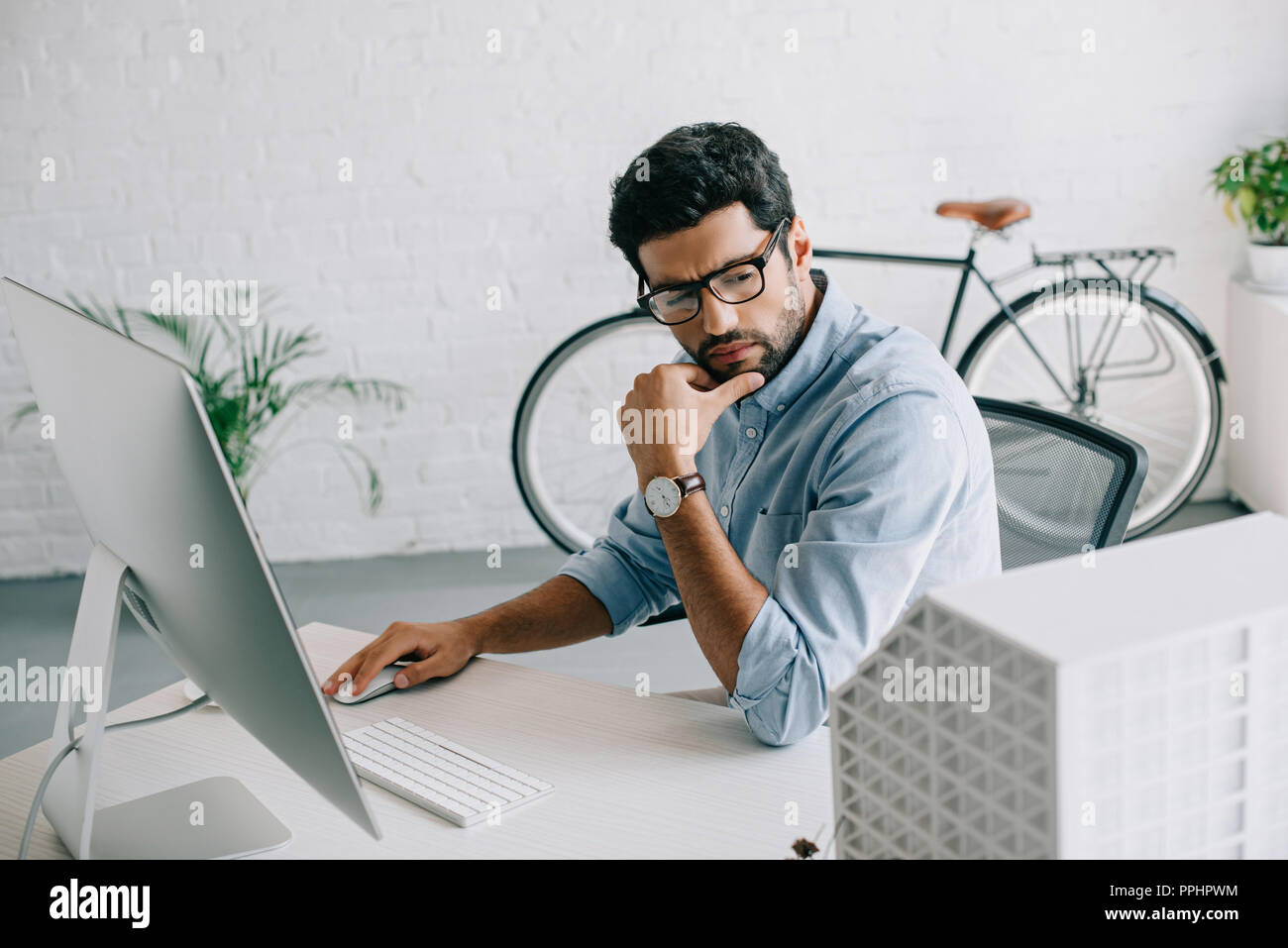 serious handsome architect using computer and looking at architecture model in office Stock Photo