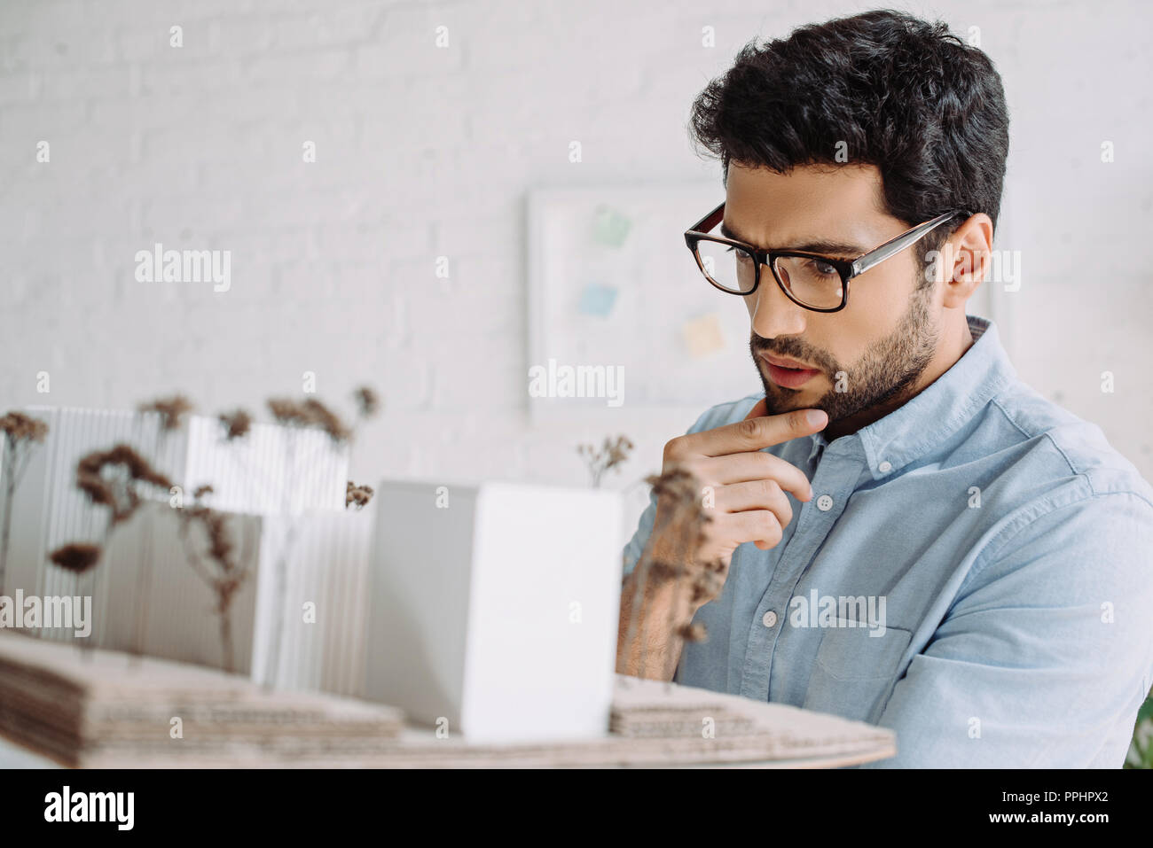 handsome pensive architect in glasses looking at architecture model in office Stock Photo