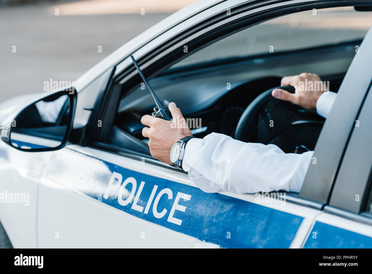cropped image of male police officer holding walkie-talkie in car ...