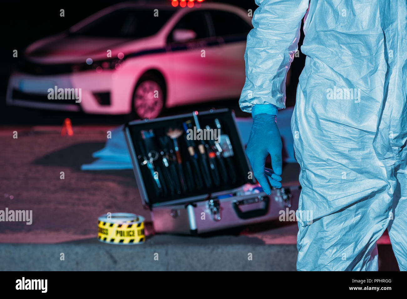cropped image of male male criminologist in protective suit standing near case with investigation tools at crime scene Stock Photo
