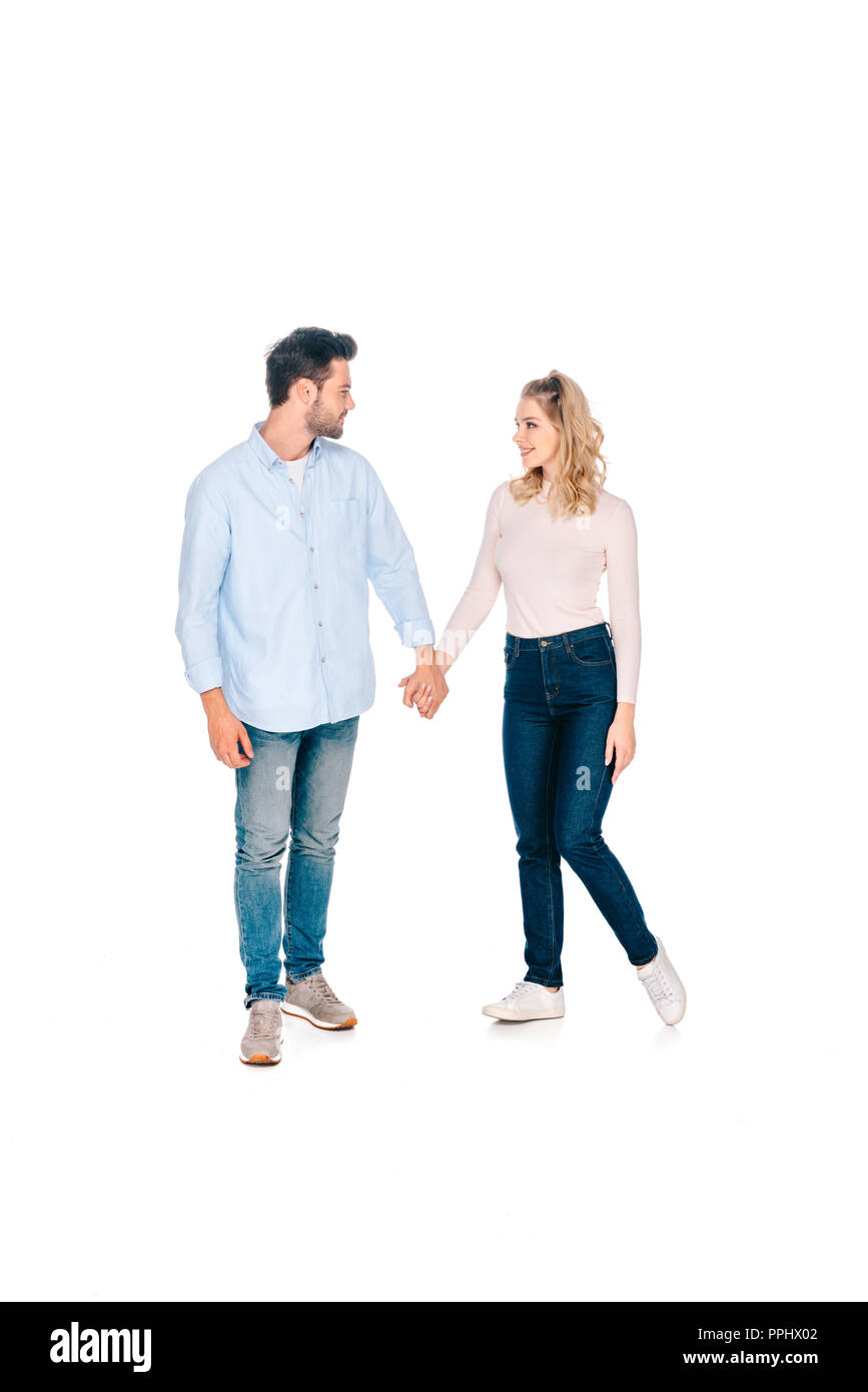 full length view of happy young couple holding hands and smiling each ...