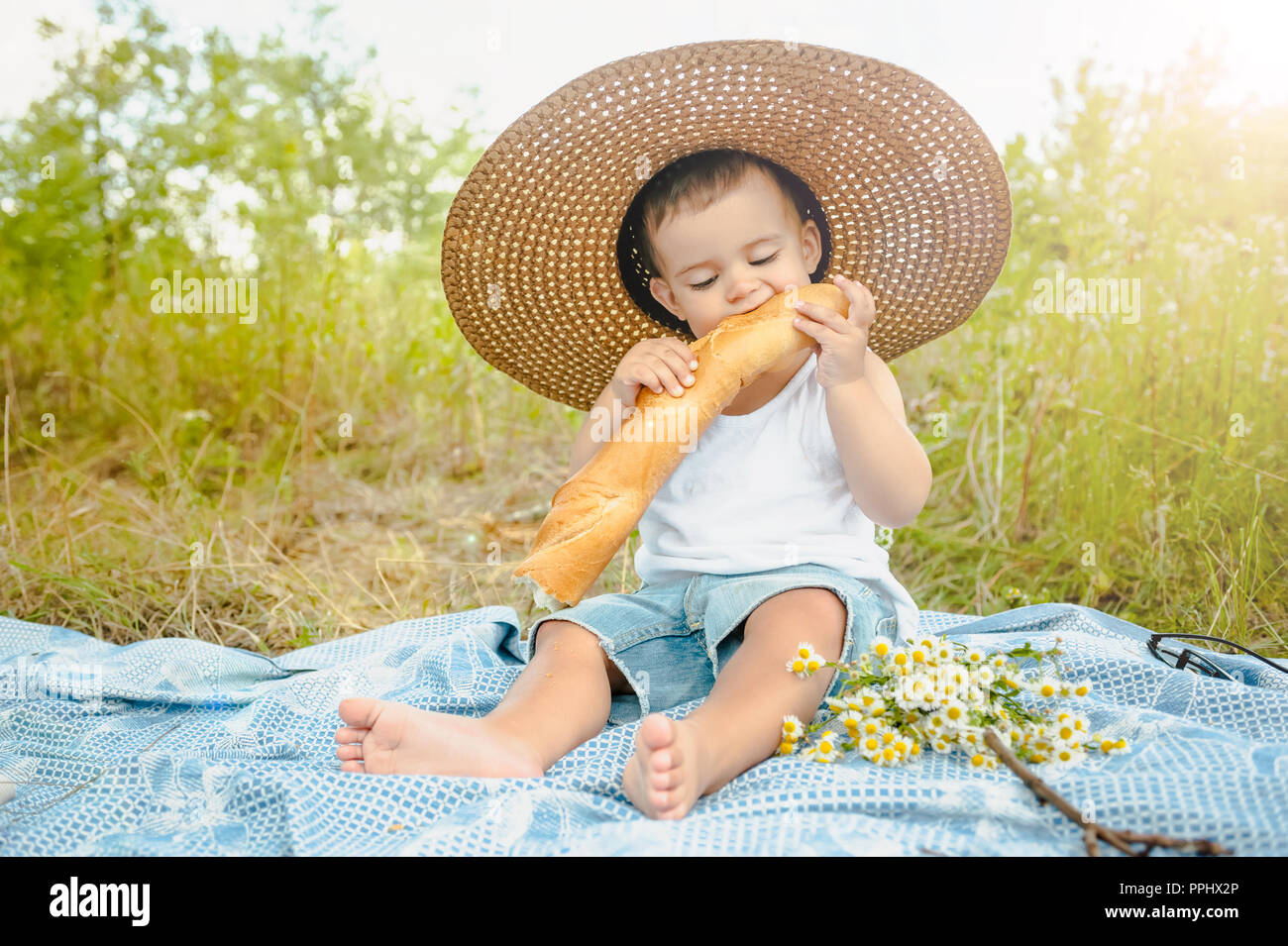 adorable toddler boy in straw hat sitting on blanket at picnic and