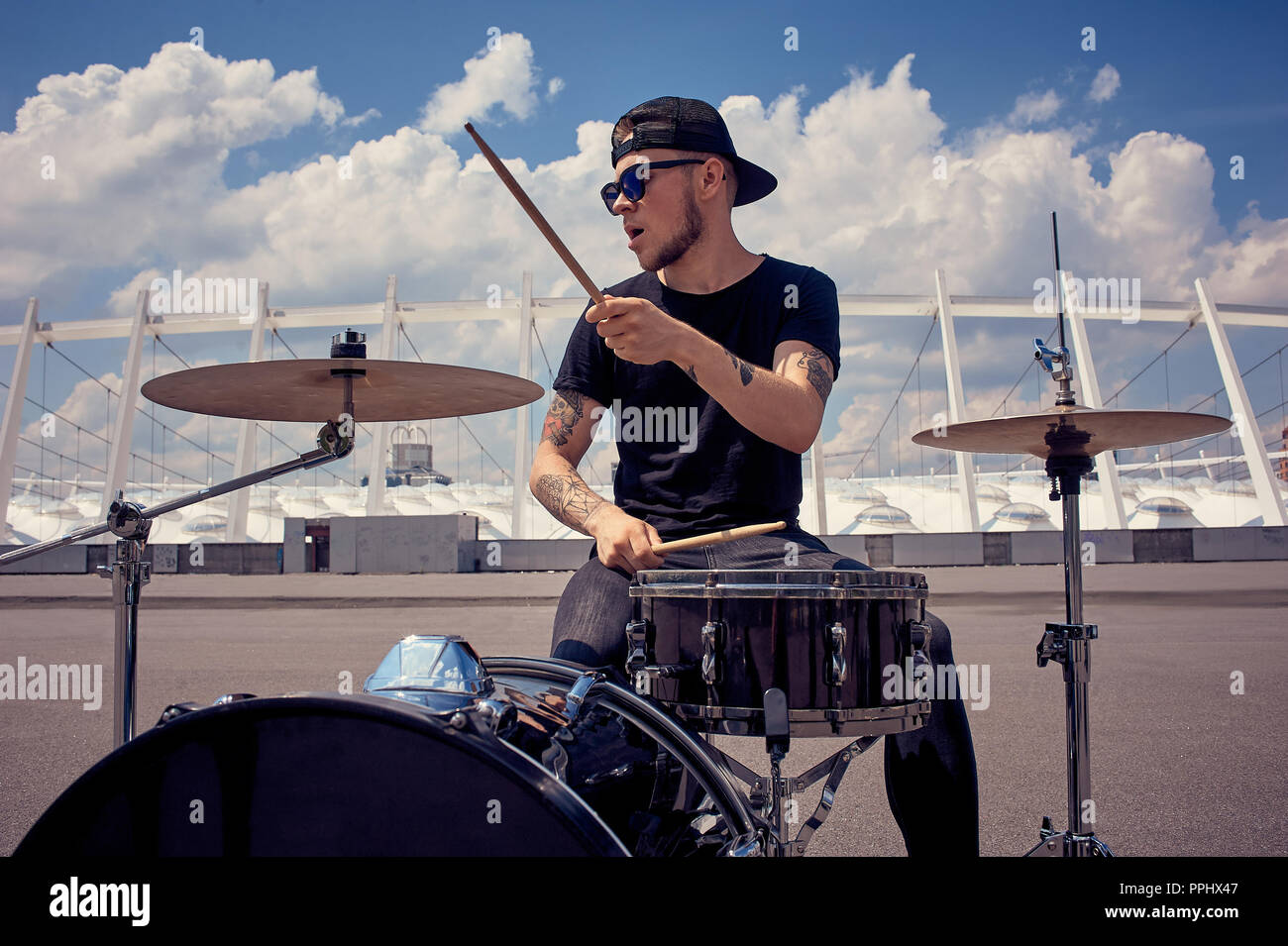young tattooed drummer in sunglasses playing drums on street Stock Photo