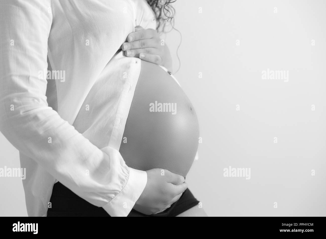 Close-up black and white studio shoot of pregnant woman touching her belly. Isolated on white background Stock Photo