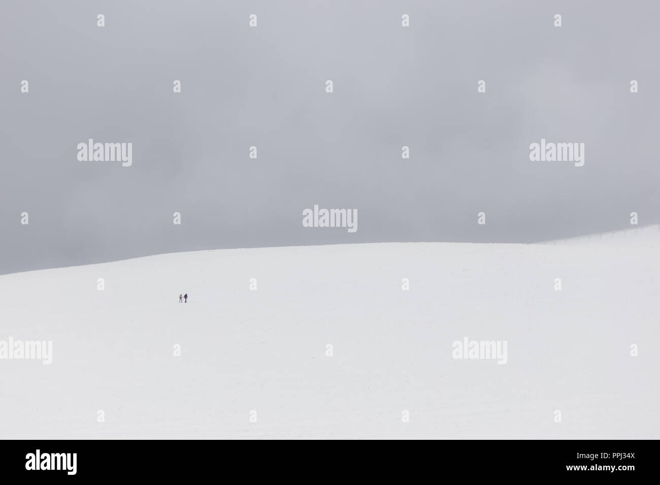 A very minimalistic view of two distant people over a mountain covered by snow Stock Photo