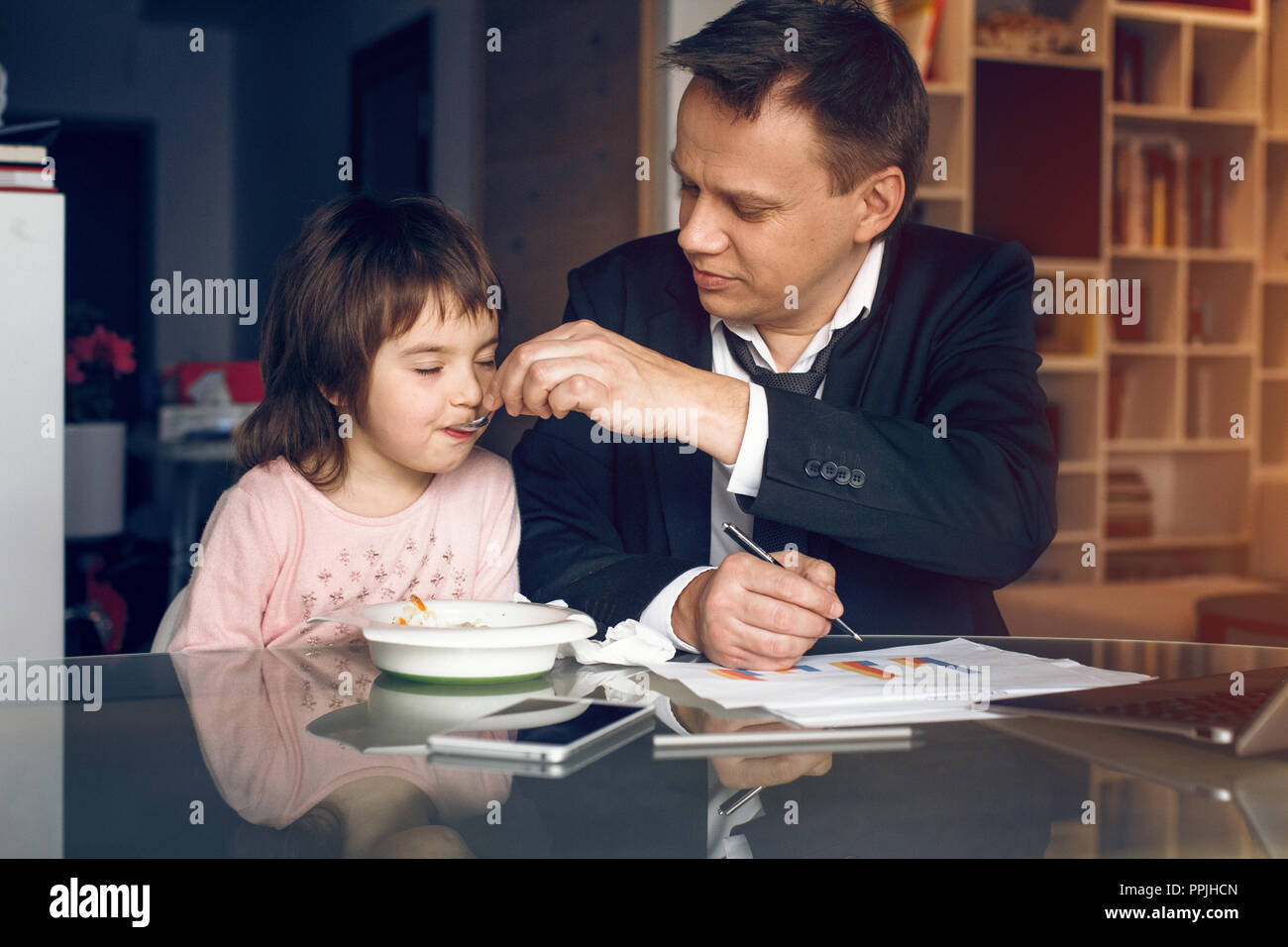 Father in suit working with papers and feeding daughter Stock Photo