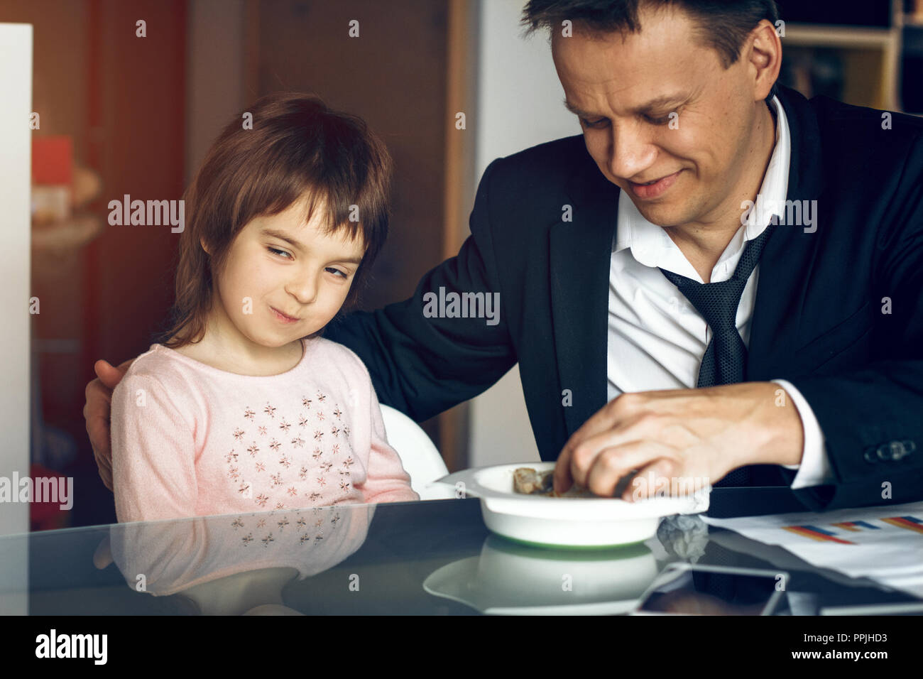 Father in suit working with papers and feeding daughter Stock Photo