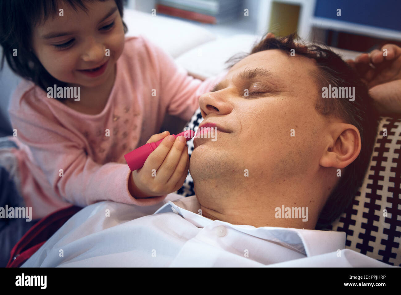 Cute little girl apply lipstick to father while he is sleeping Stock Photo