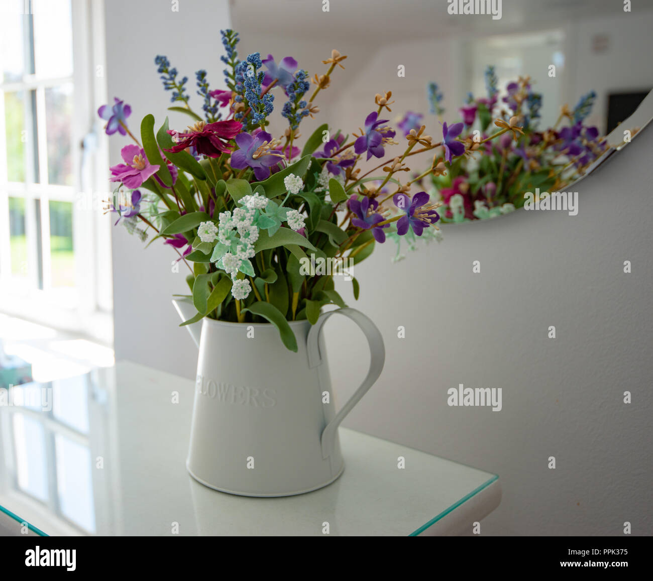 selection of natural/wild colourful looking flowers displayed in a white jug in natural light against a white background Stock Photo